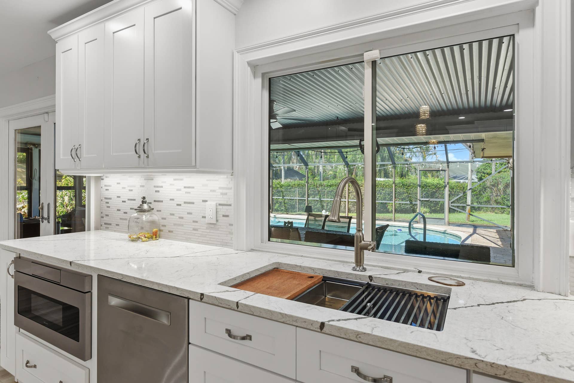 3098 SE BUR Street, Port St Lucie, FL 34952 Enjoy picturesque pool views right from the kitchen! Features a double-basin stainless steel sink with built-in accessories, high-arc faucet, decorative tile backsplash, and beautiful marble-look countertops. A perfect blend of luxury and functionality!