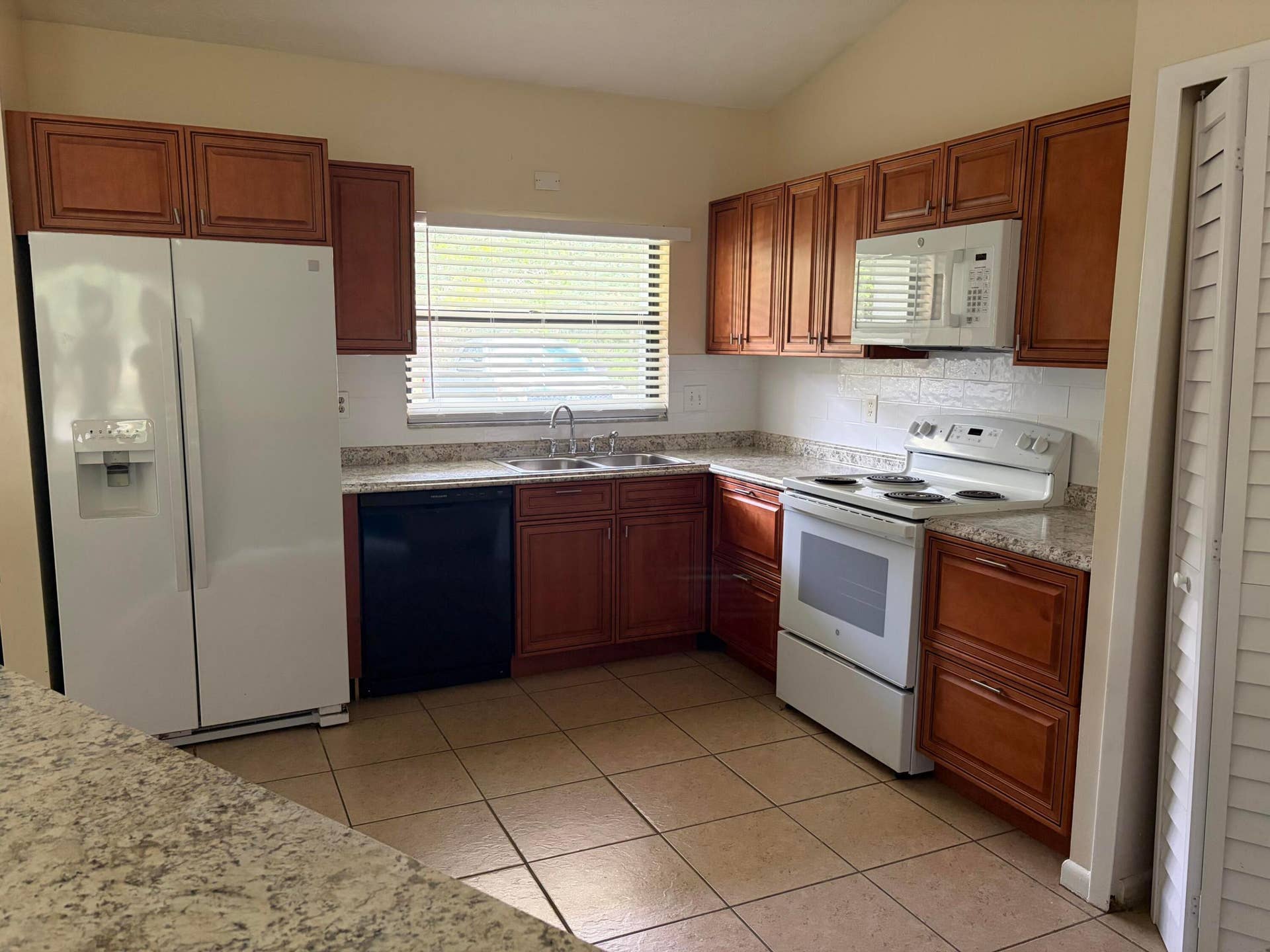 Kitchen featuring wood cabinetry, stone-finish countertops, tile flooring, and integrated white appliances