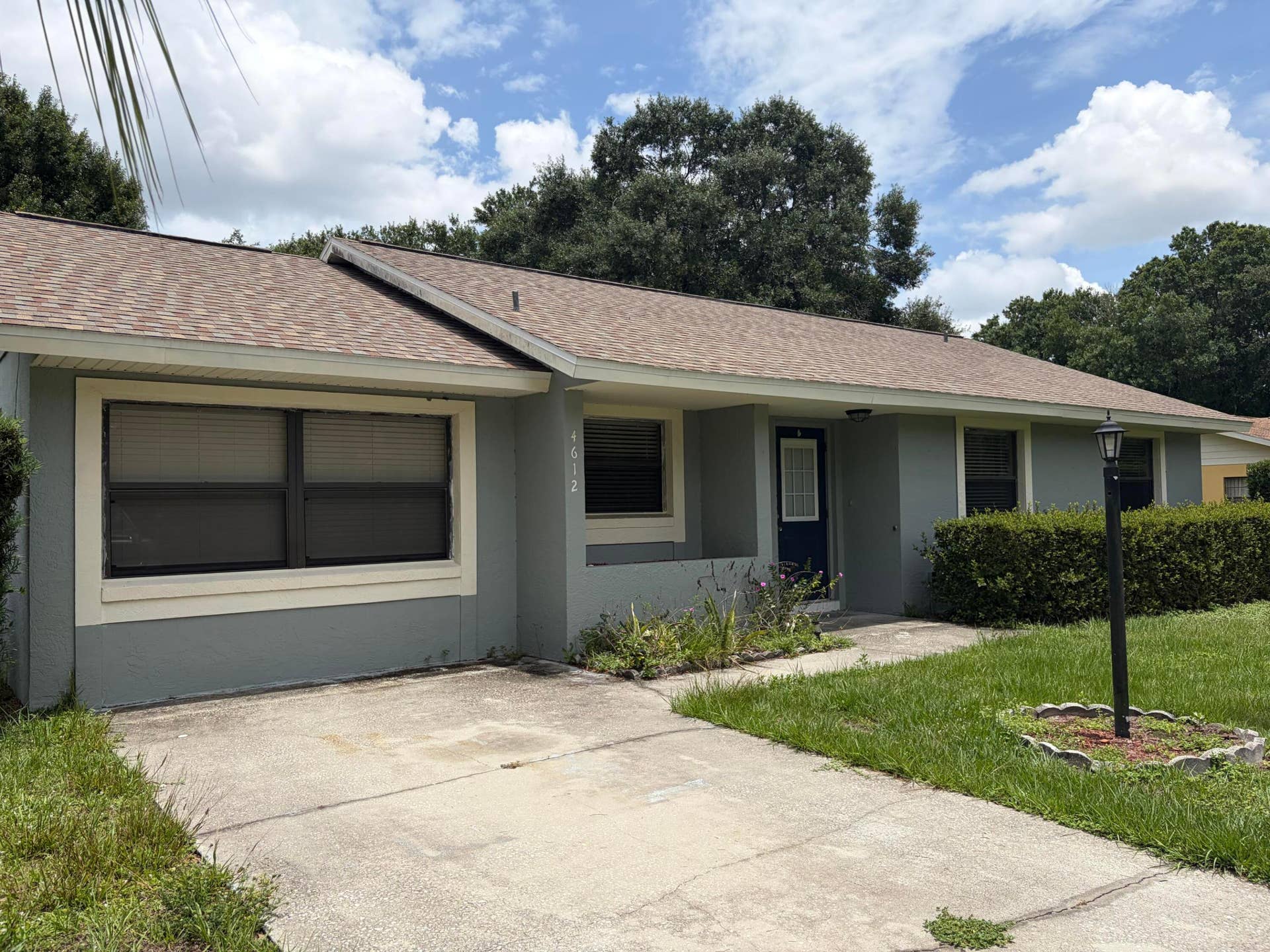 Single-story exterior featuring a neutral-toned facade, shingled roof, concrete driveway, and attached exterior lighting fixture