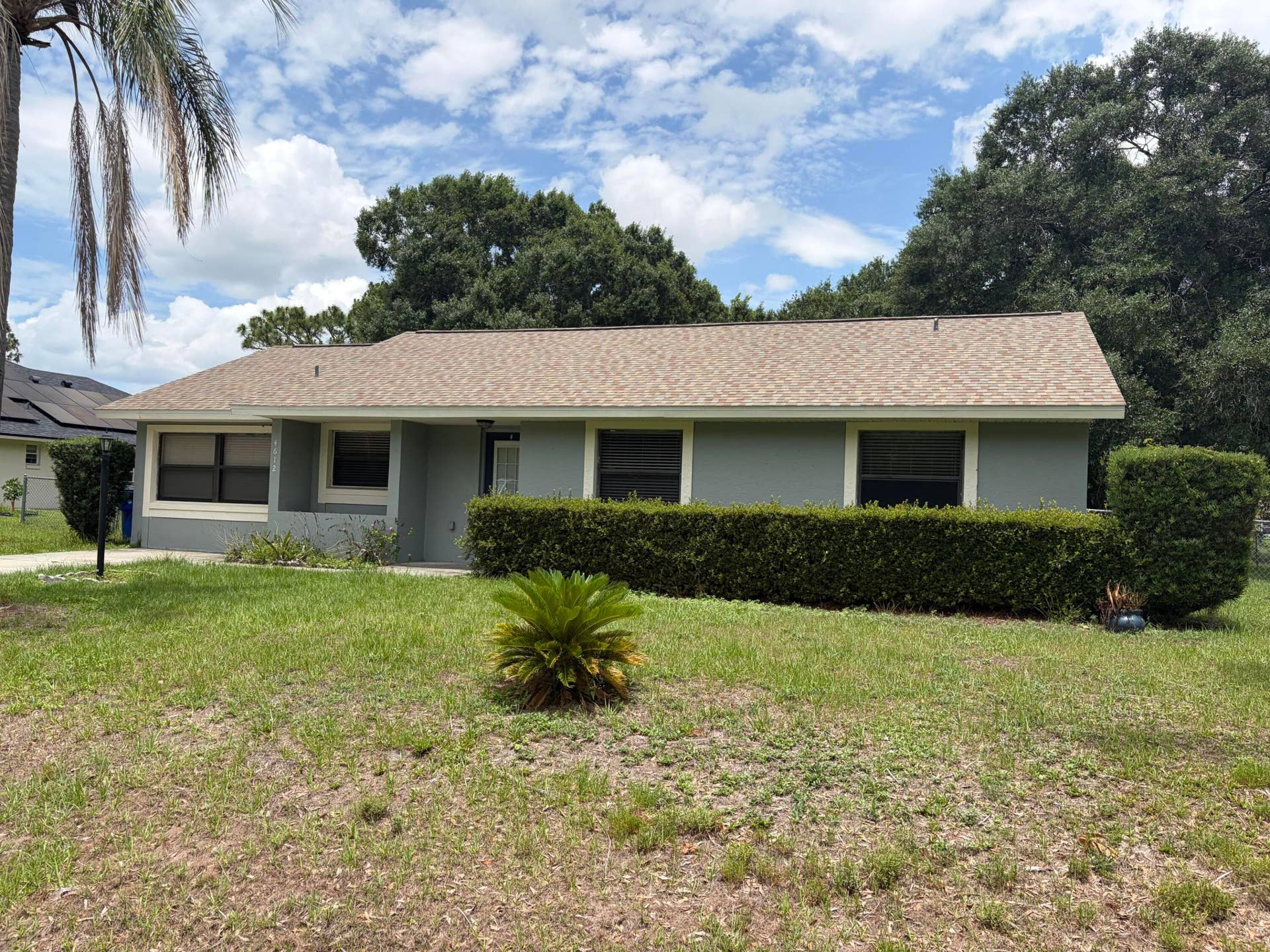 Single-story exterior featuring a shingled roof, neutral-toned siding, and established landscaping with manicured shrubbery