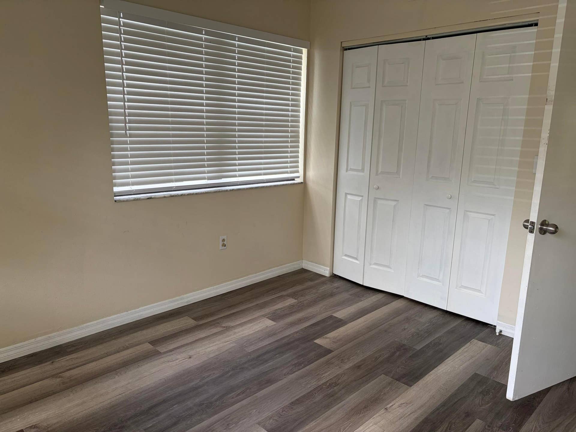 Room featuring wood-finish flooring, a bi-fold closet with paneled doors, and a window with horizontal blinds