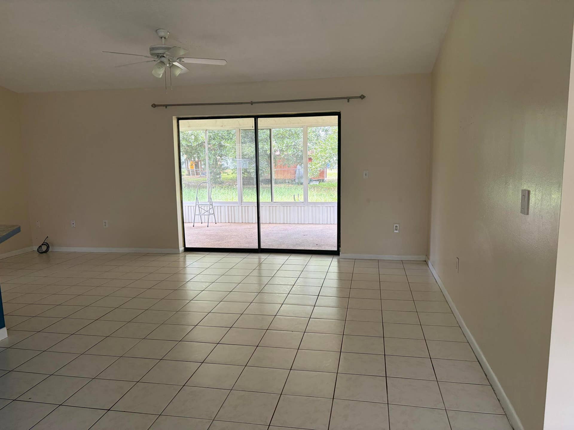 Spacious interior featuring neutral ceramic tile flooring, a central ceiling fan with integrated lighting, and sliding glass doors that open to an enclosed patio