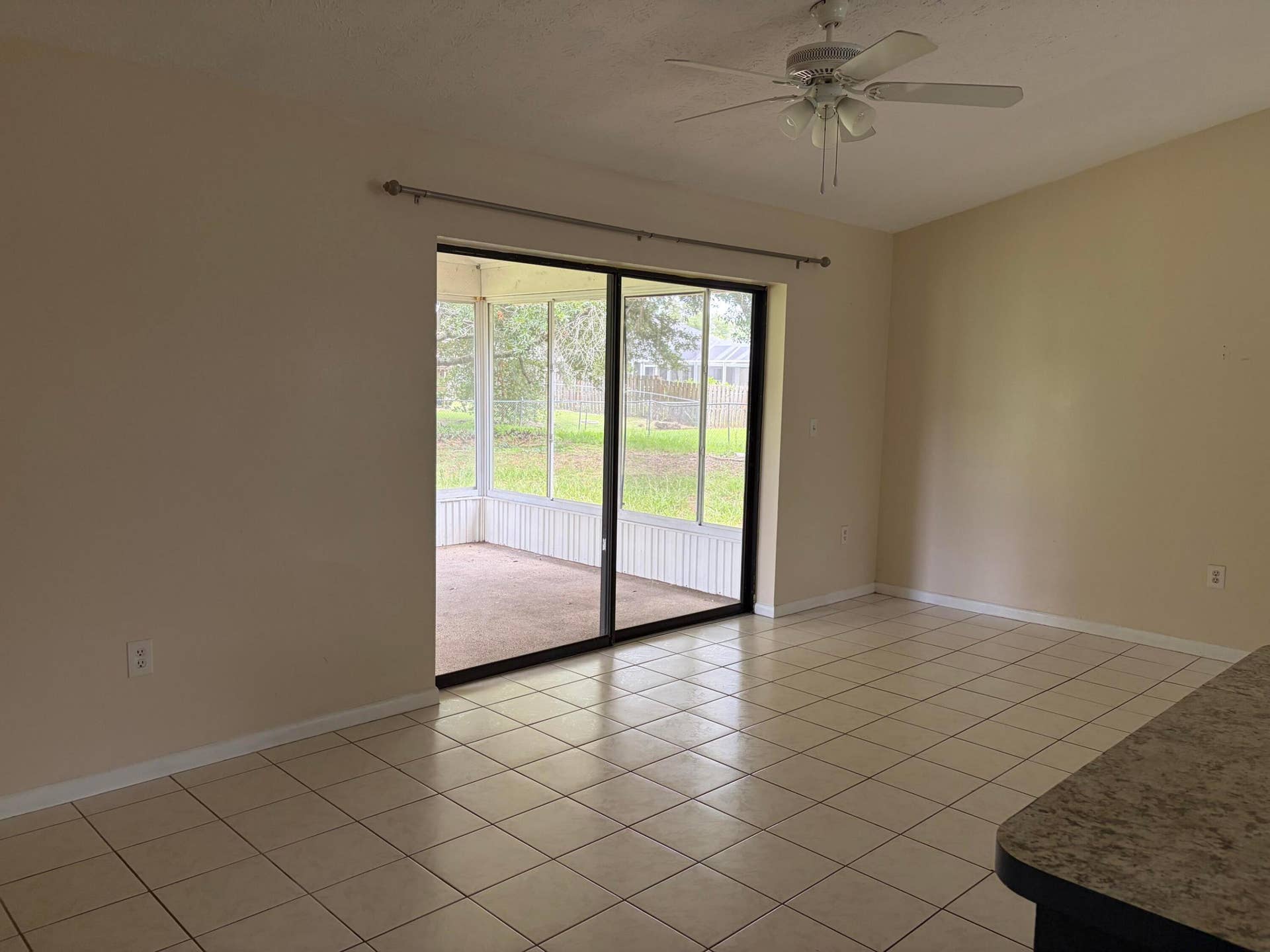 Ceramic tile flooring, vaulted ceiling with a white overhead fan, and sliding glass doors opening to a screened-in lanai