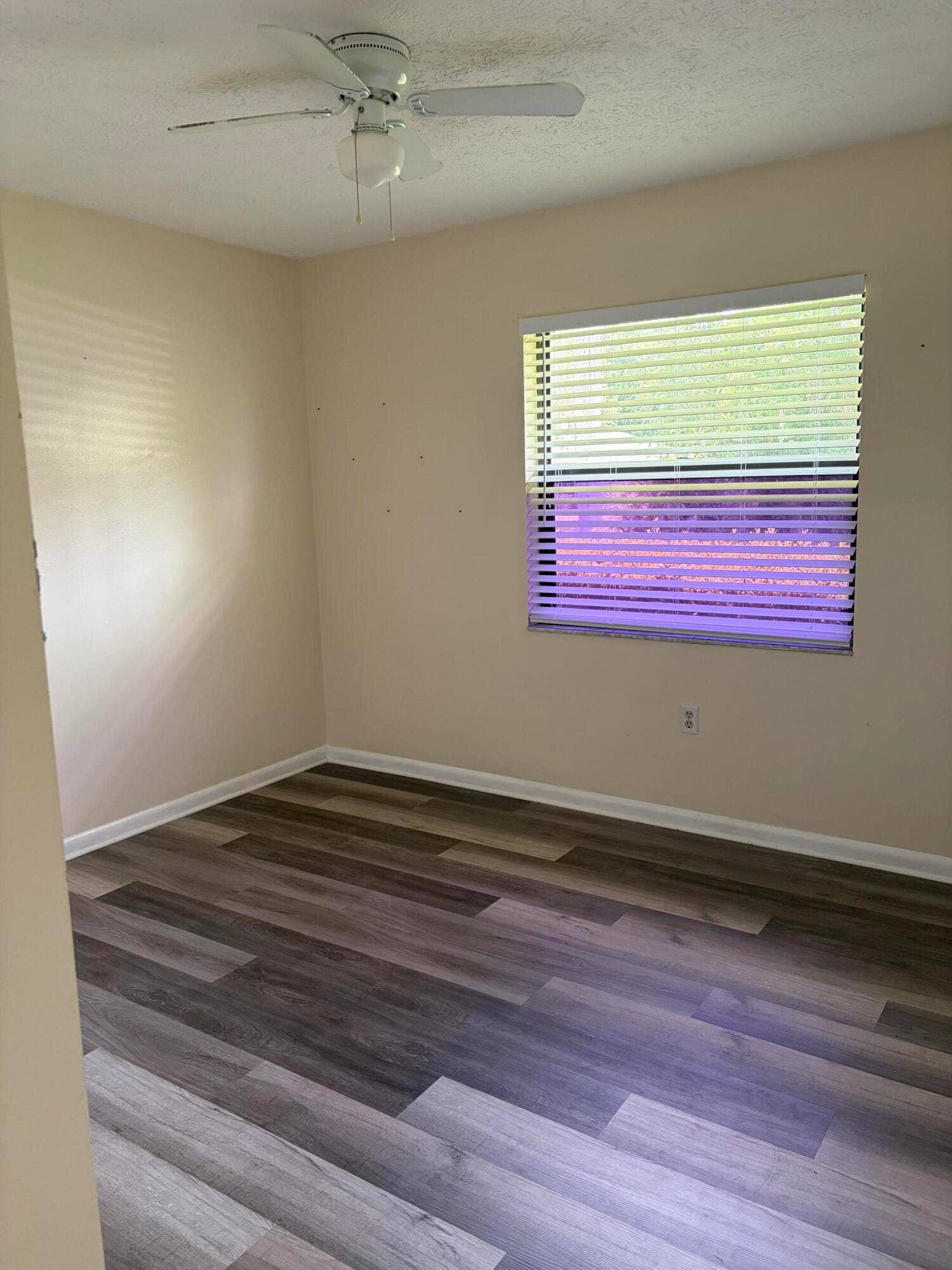 Room featuring wood-finish flooring, a white ceiling fan with integrated lighting, and a window fitted with horizontal blinds