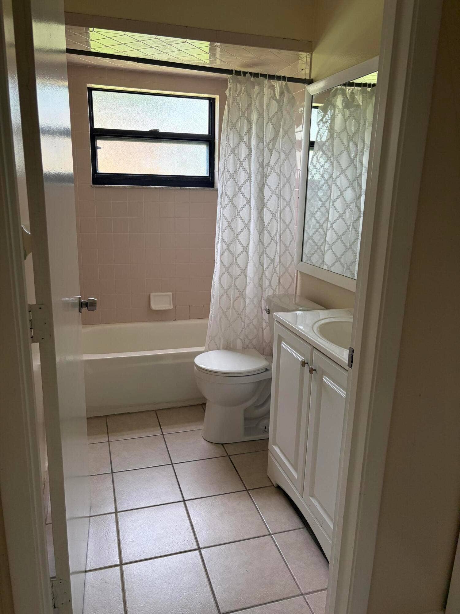Bathroom featuring a white vanity cabinet with a integrated sink, ceramic tile flooring, a bathtub with wall-mounted soap dish, and a framed mirror