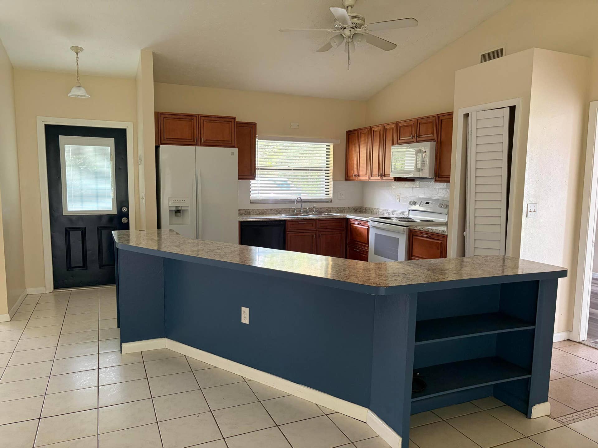 Kitchen featuring wood cabinetry, solid-surface countertops, built-in shelving, vaulted ceiling, and ceramic tile flooring