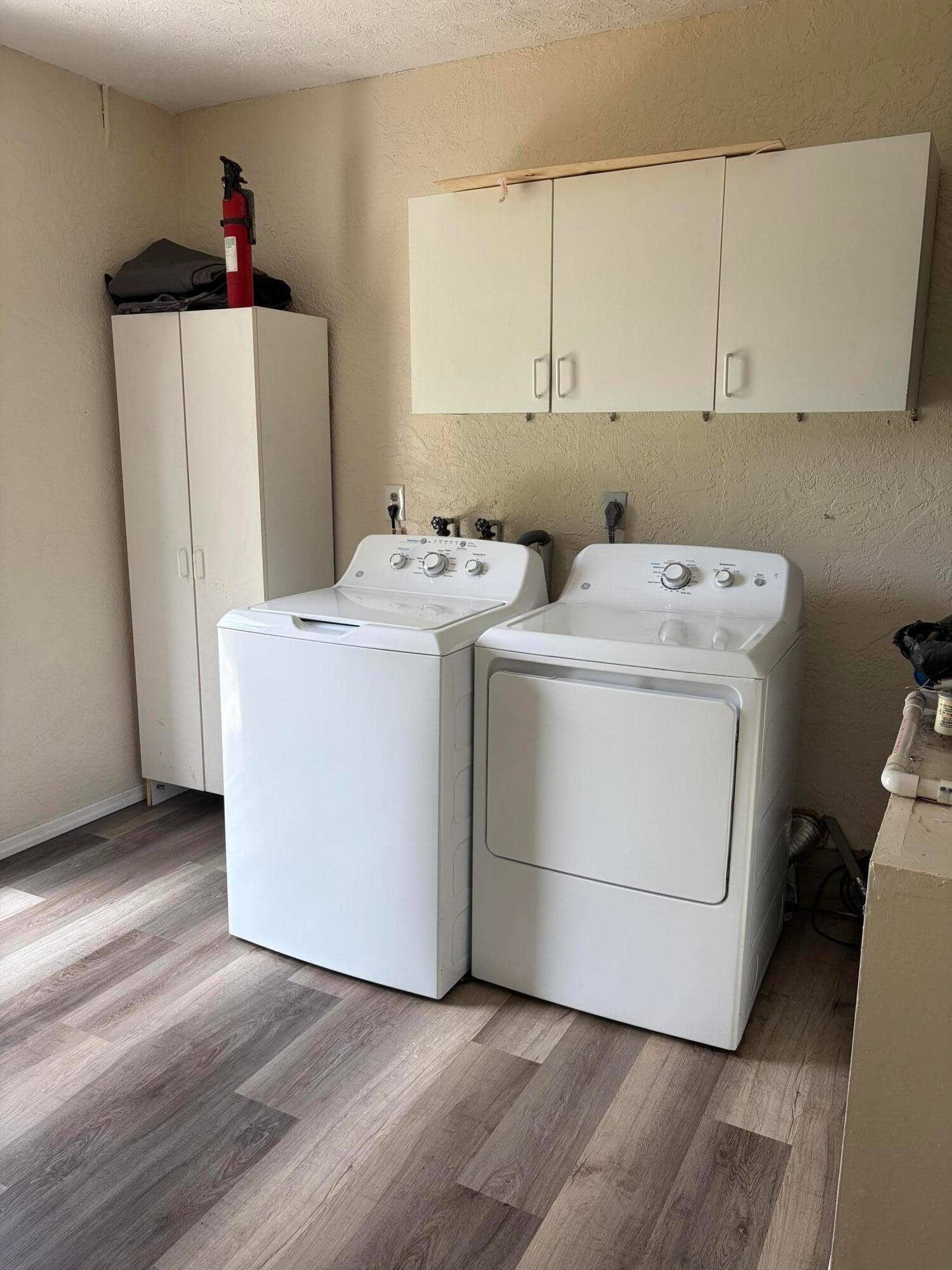 Utility space featuring wood-finish flooring, white built-in wall cabinetry, and a tall white storage cabinet