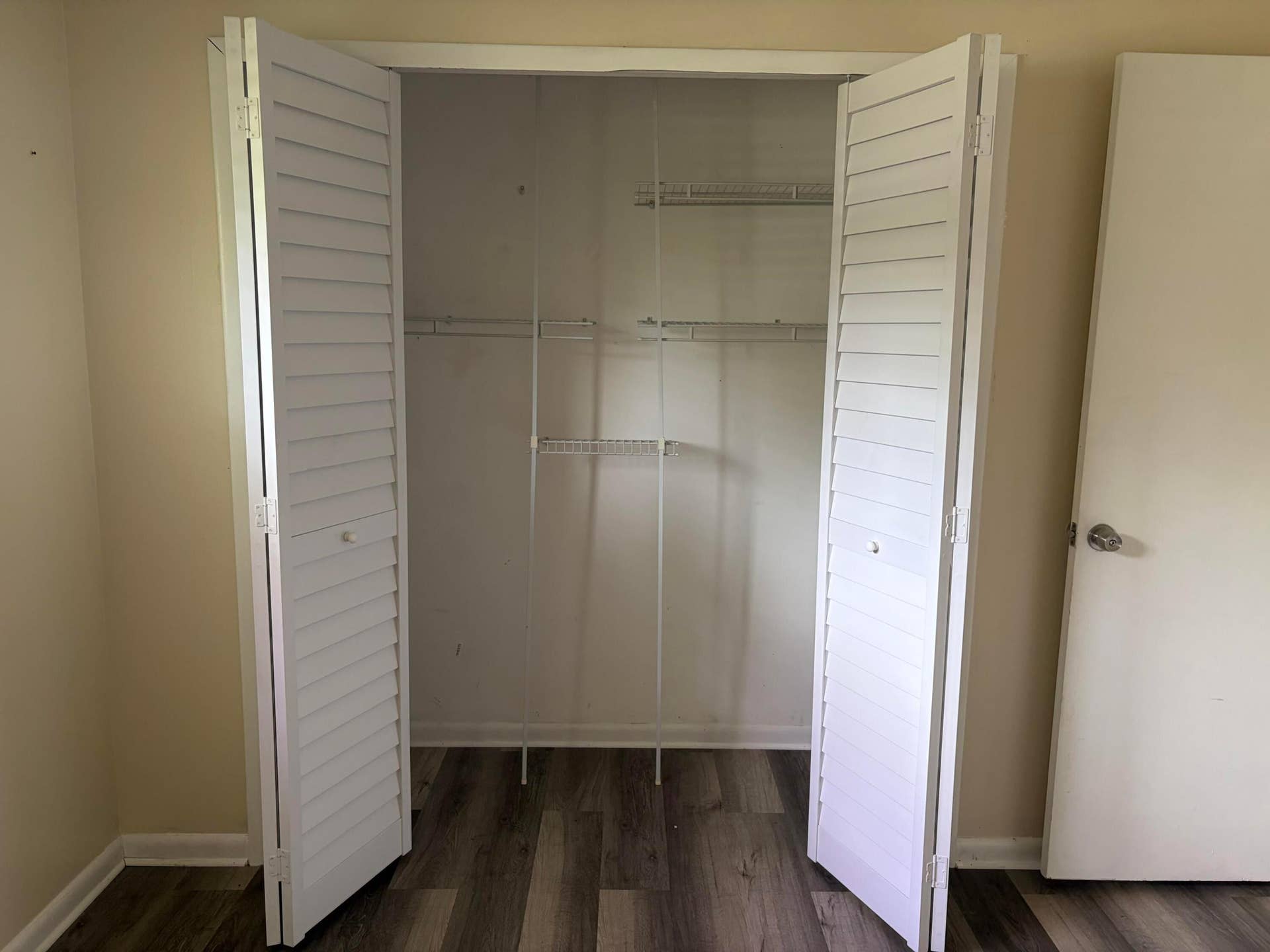 Reach-in closet featuring white louvered bi-fold doors, white wire shelving, and wood-finish flooring