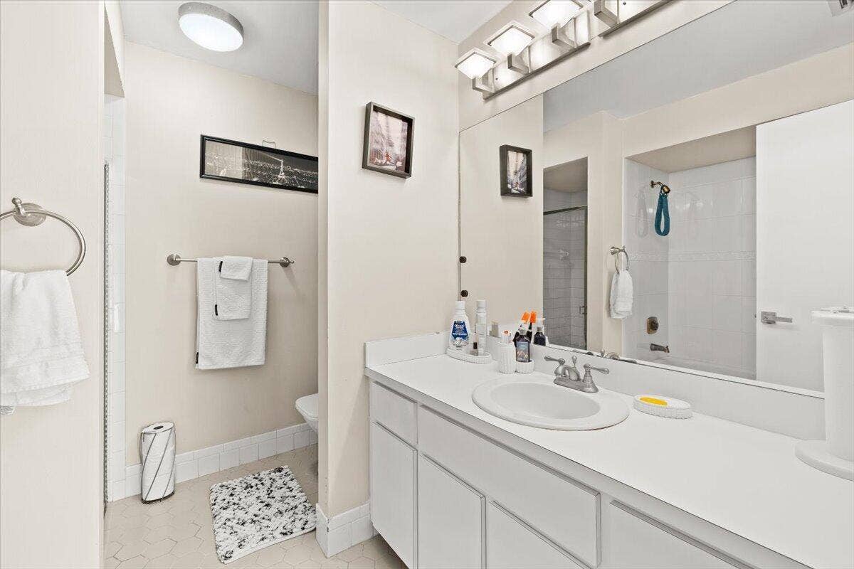 Bathroom featuring a vanity with a white countertop and oval under-mount sink, full-width wall mirror, four-light vanity fixture, and a tub-shower combination with white wall tile