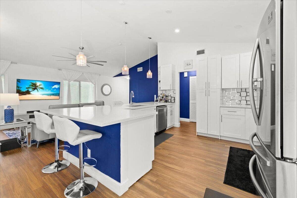 Kitchen featuring wood-finish flooring, a central island with a solid surface countertop, white shaker-style cabinetry, stainless steel appliances, and multi-pendant lighting