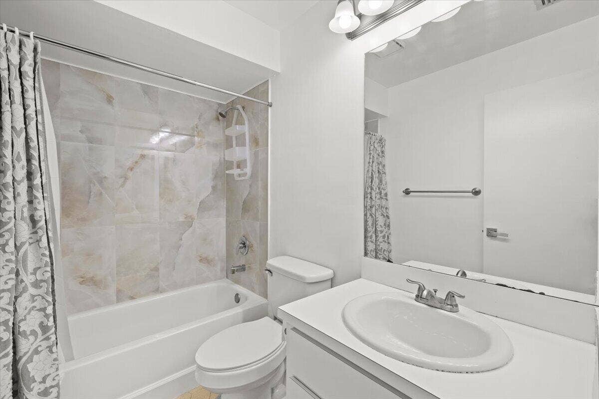 Bathroom featuring a vanity with an integrated sink, a large wall-mounted mirror, a tub-shower combination with decorative tile surround, and overhead lighting