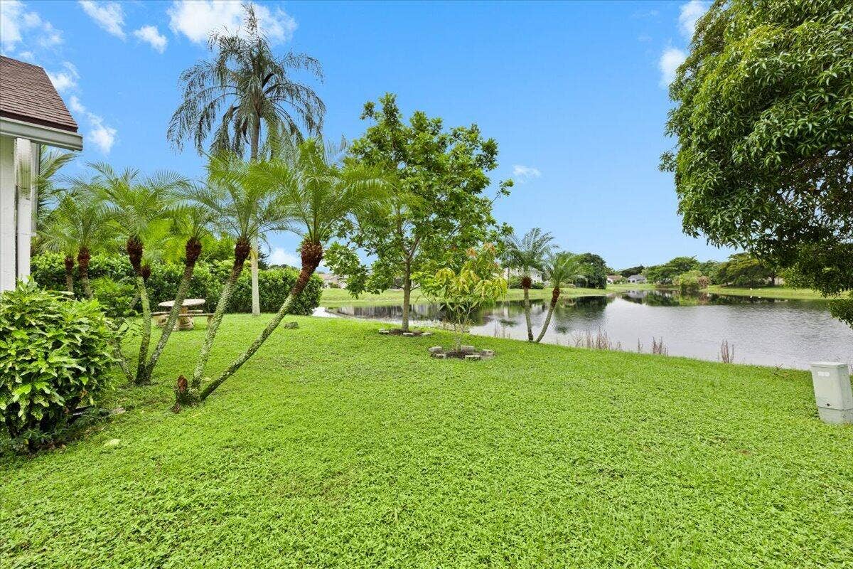 Expansive green lawn featuring mature palm trees, established landscaping, and direct frontage to a pond