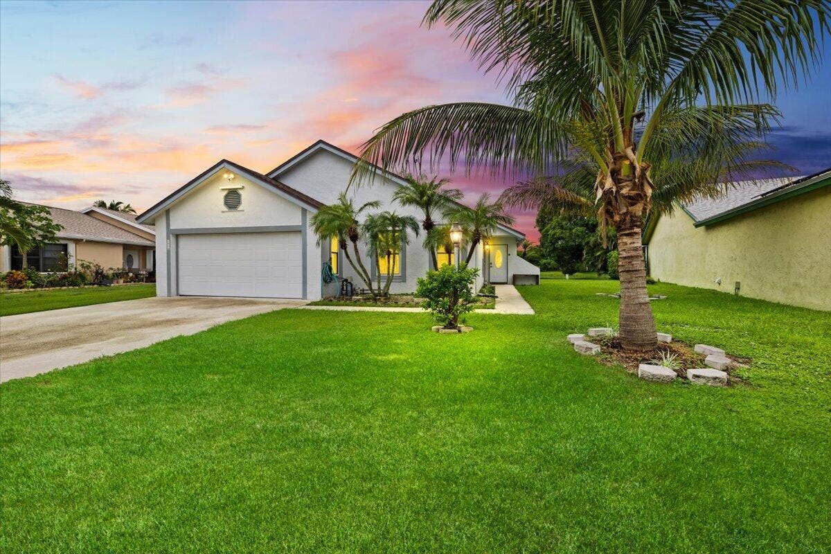 Single-story residence featuring a front-facing attached garage, concrete driveway, and landscaping with mature palm trees