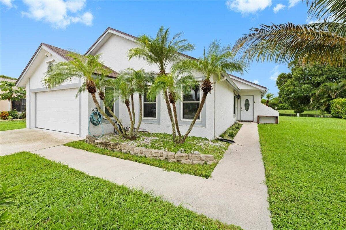 Exterior featuring white stucco facade, a two-car garage, stone-block garden border, and palm tree landscaping