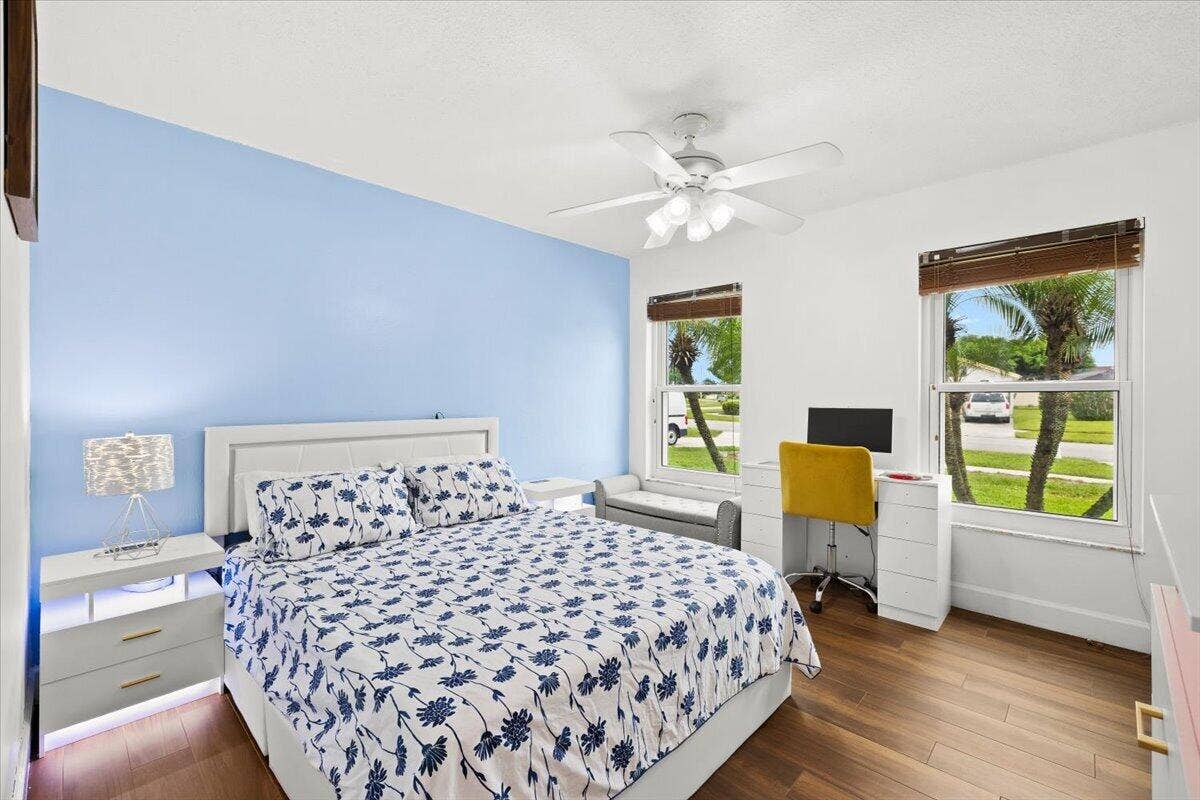 Wood-finish flooring, ceiling fan with integrated lighting, dual windows with wood-tone blinds, and a blue accent wall