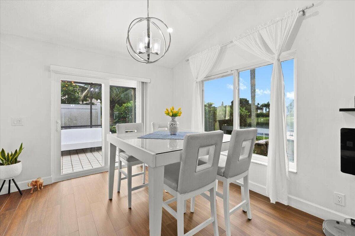 Vaulted ceilings, wood-finish flooring, spherical chandelier, large glass sliding doors, and windows featuring exterior greenery