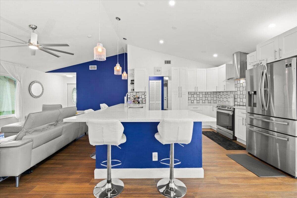 Kitchen featuring white cabinetry, a sprawling center island with a solid surface countertop, stainless steel appliances, a geometric patterned backsplash, and wood-finish flooring