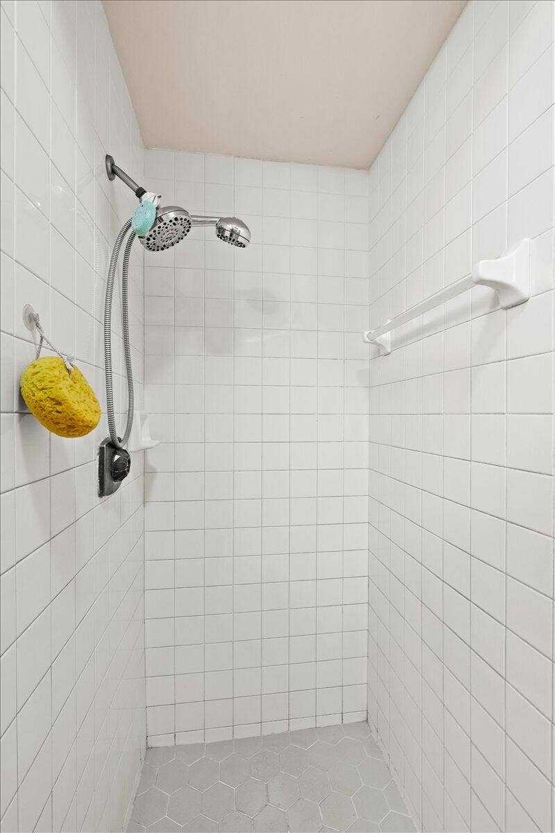 Walk-in shower featuring white square wall tiling, a hand-held showerhead on an adjustable slide bar, a mounted towel bar, and a neutral-toned hexagonal tile floor