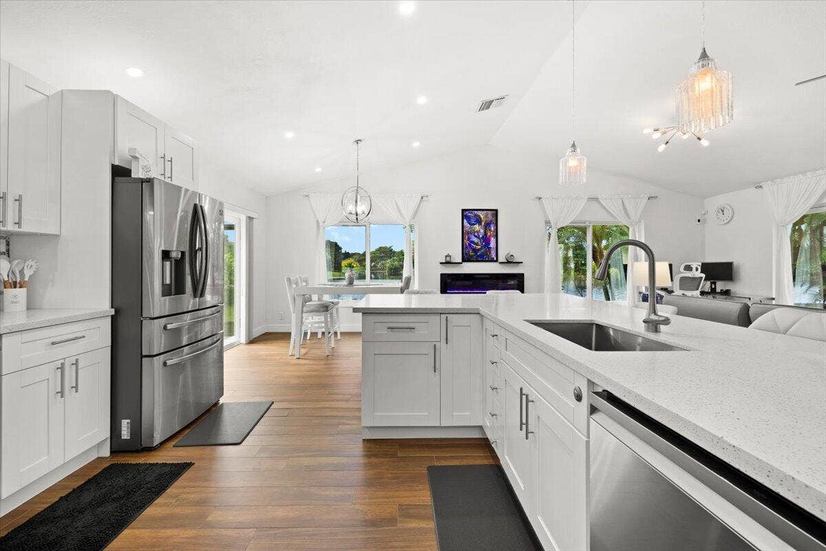 Kitchen featuring white cabinetry, quartz countertops, stainless steel appliances, wood-finish flooring, and vaulted ceilings with recessed lighting