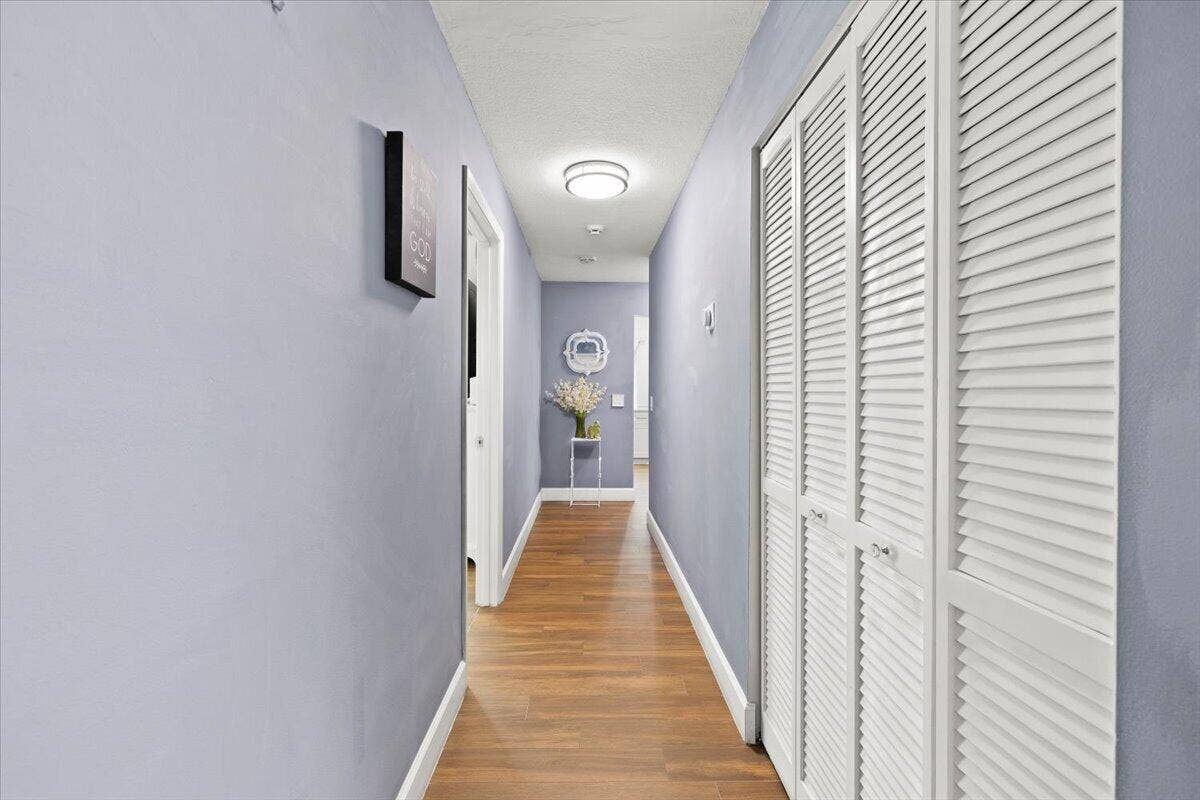 Hallway featuring wood-finish flooring, crisp white trim, and white bi-fold louvered closet doors