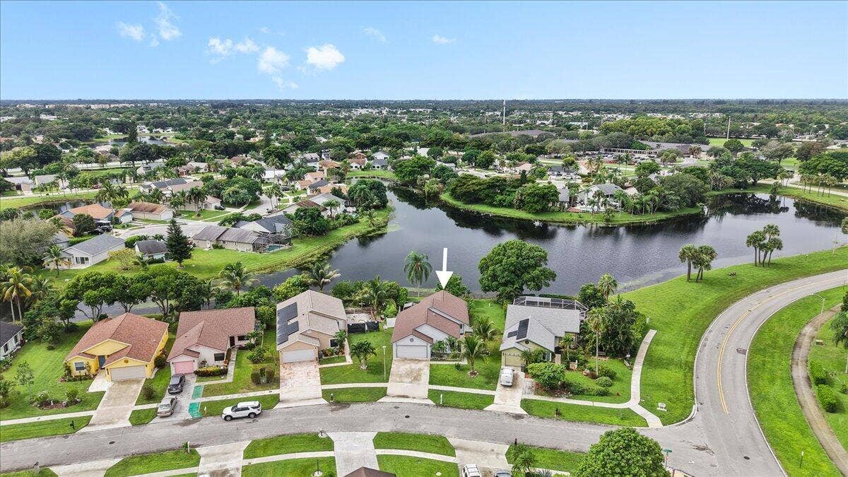 Aerial perspective featuring a single-story residence with a multi-gable roofline, attached two-car garage, solar panels, and waterfront positioning