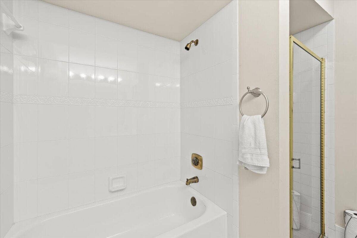 Full-height white wall tile, built-in recessed soap dish, metallic shower and tub fixtures, and a separate glass-enclosed shower stall with a gold-tone frame