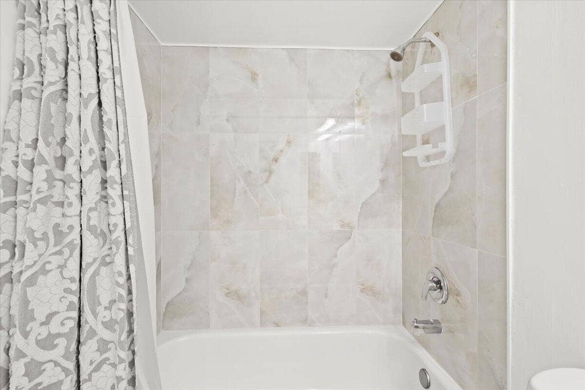 Bathtub alcove featuring full-height stone-finish wall tile, a single-handle chrome shower faucet, and a wall-mounted chrome tub spout