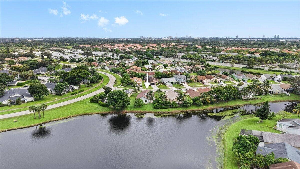 Aerial perspective featuring a waterfront lot, expansive green space, and mature landscaping within a suburban community