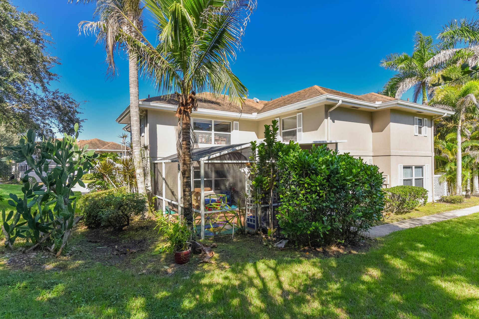 3233 SW SUNSET TRACE Circle, Palm City, FL 34990 Two-story exterior featuring a screened-in lanai, stucco siding, a shingled hip roof, and lush landscaping