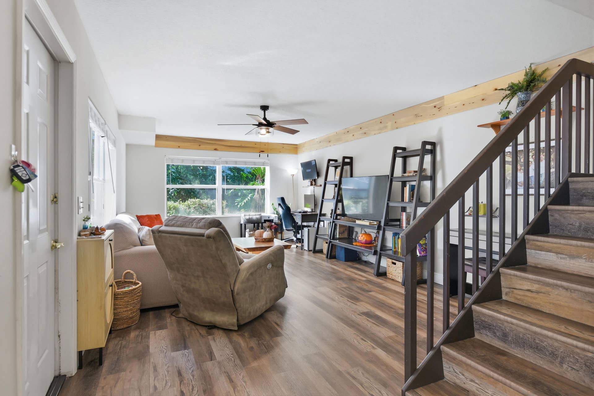 3233 SW SUNSET TRACE Circle, Palm City, FL 34990 Living area featuring wood-finish flooring, exposed natural wood ceiling beams, a ceiling fan with integrated lighting, and a staircase with dark wood handrails and balusters