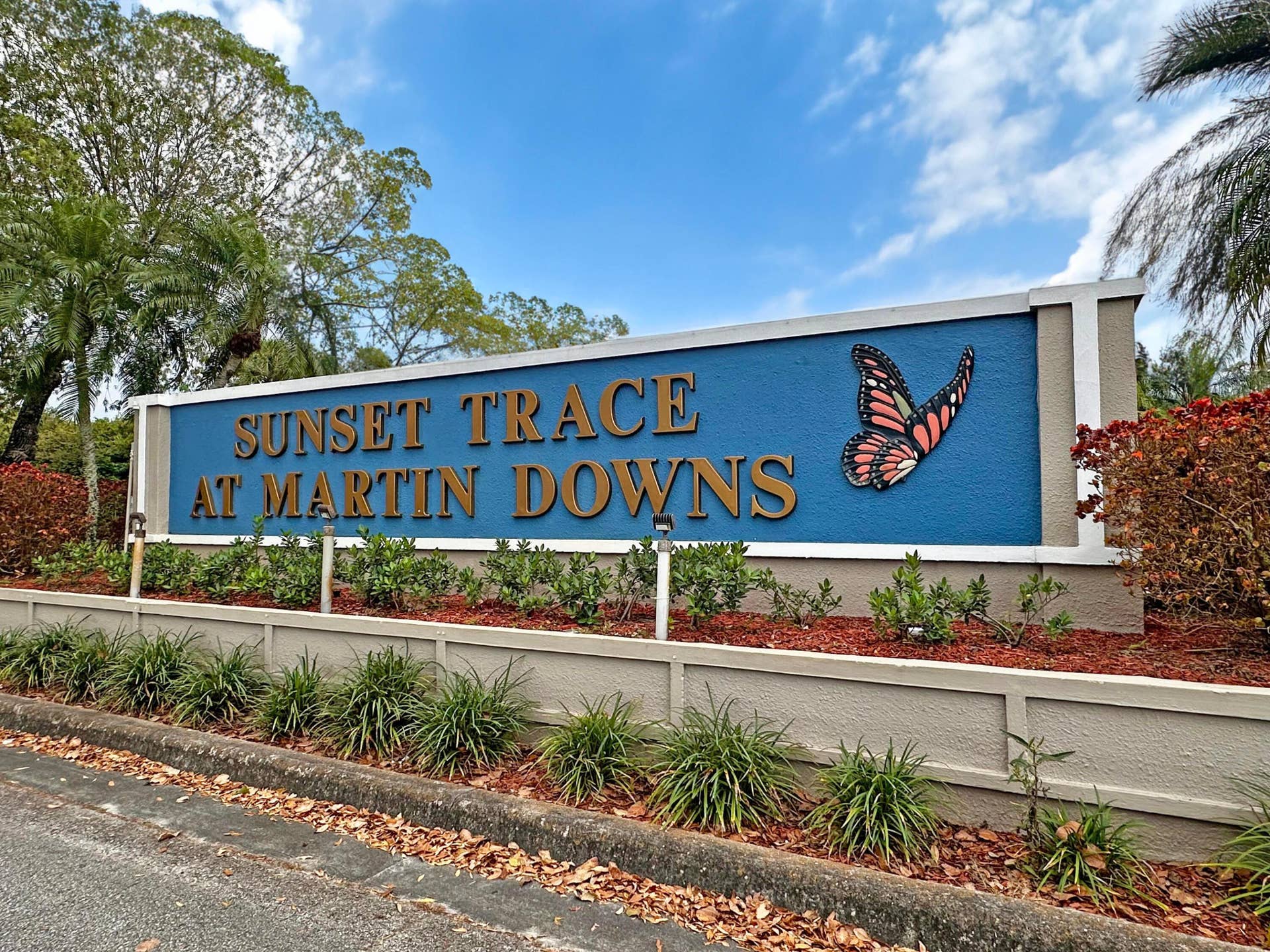 3233 SW SUNSET TRACE Circle, Palm City, FL 34990 Community entrance monument sign featuring stucco siding, integrated landscape lighting, and decorative butterfly accent