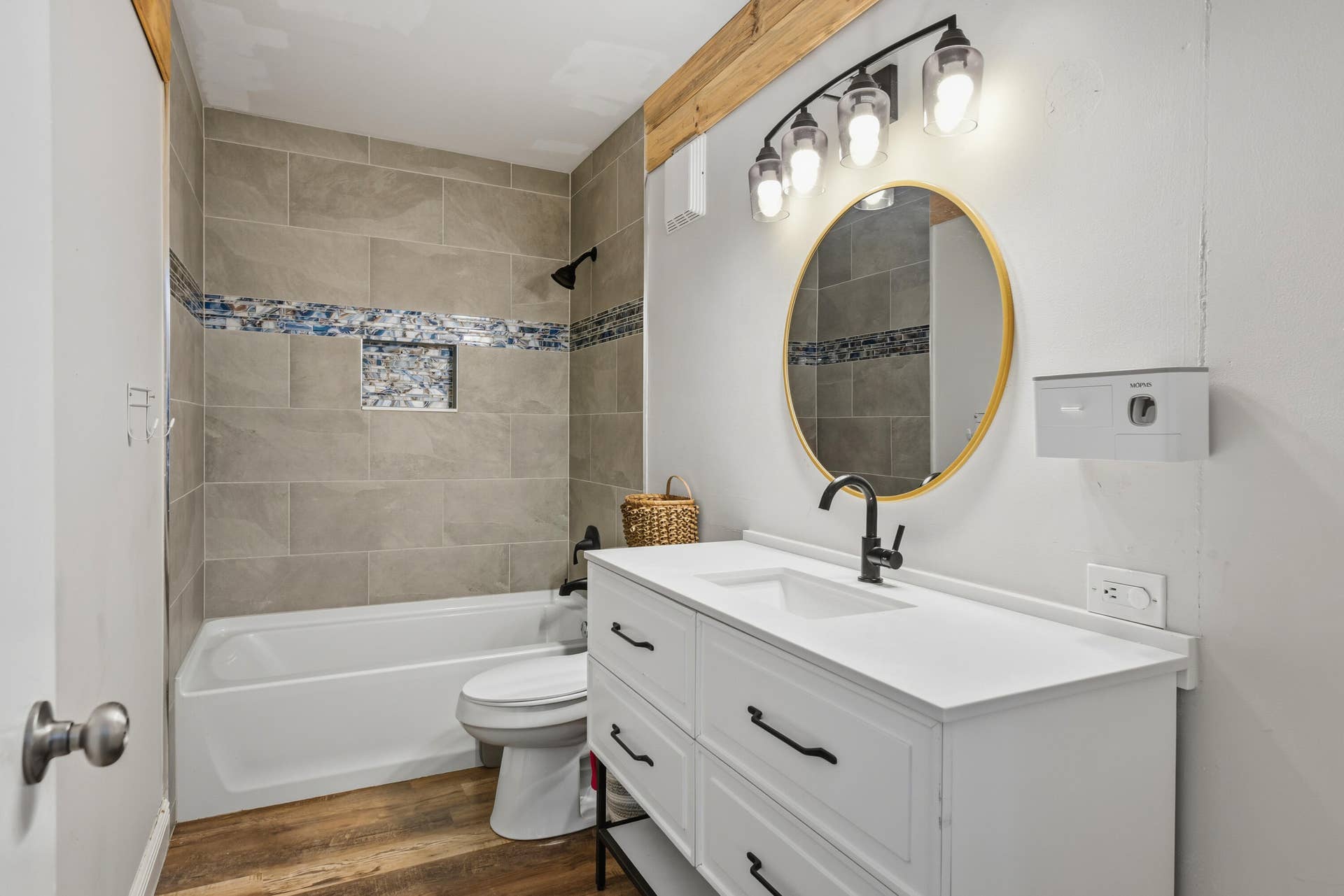 3233 SW SUNSET TRACE Circle, Palm City, FL 34990 Bathroom featuring wood-finish flooring, white vanity with matte black hardware, round mirror with metallic trim, and tub-shower combination with decorative tile inlay