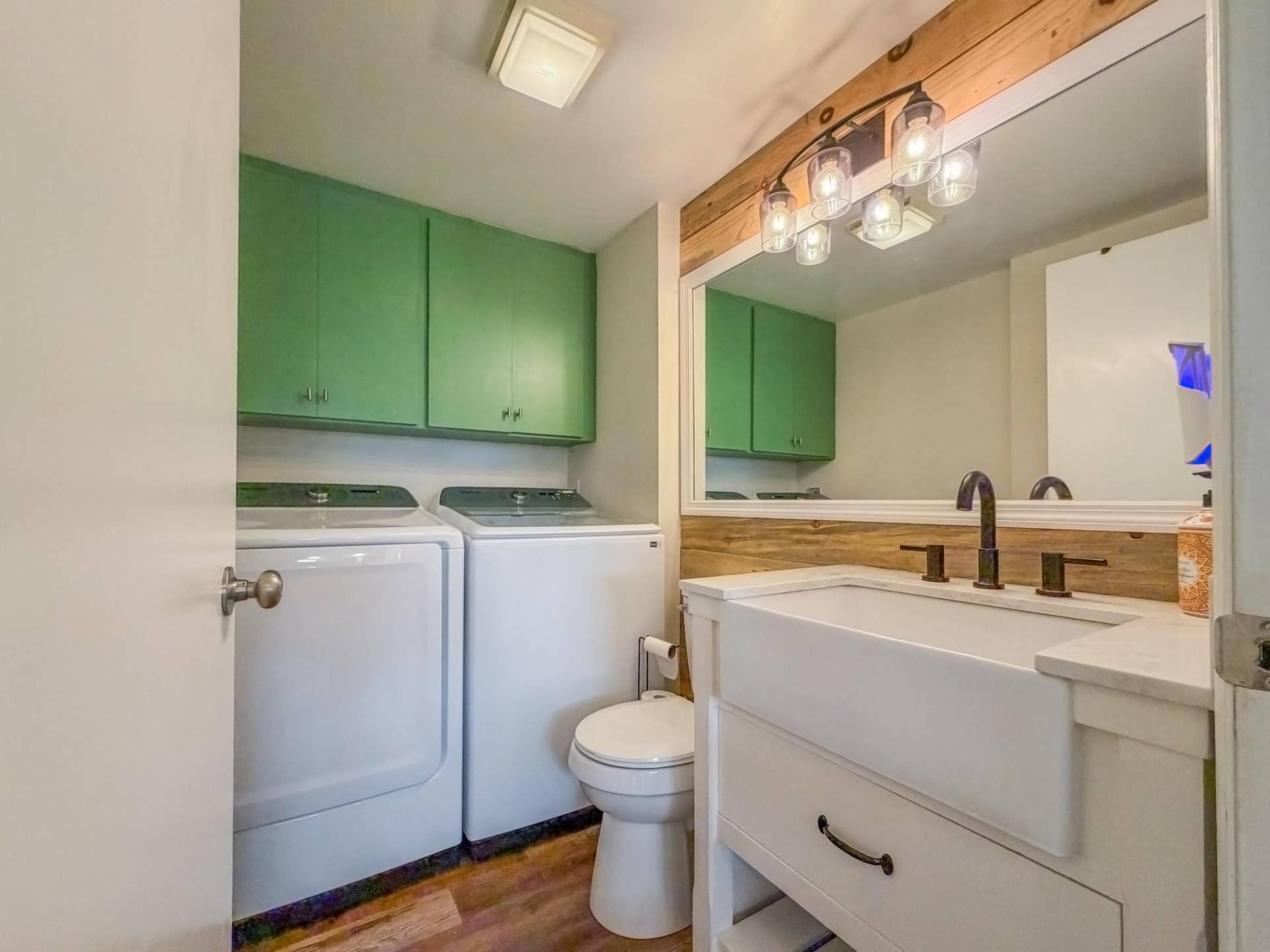 3233 SW SUNSET TRACE Circle, Palm City, FL 34990 Farmhouse-style vanity with apron-front sink and matte black faucet, wood-paneled wall accent, glass globe vanity lighting, and wall-mounted green cabinetry
