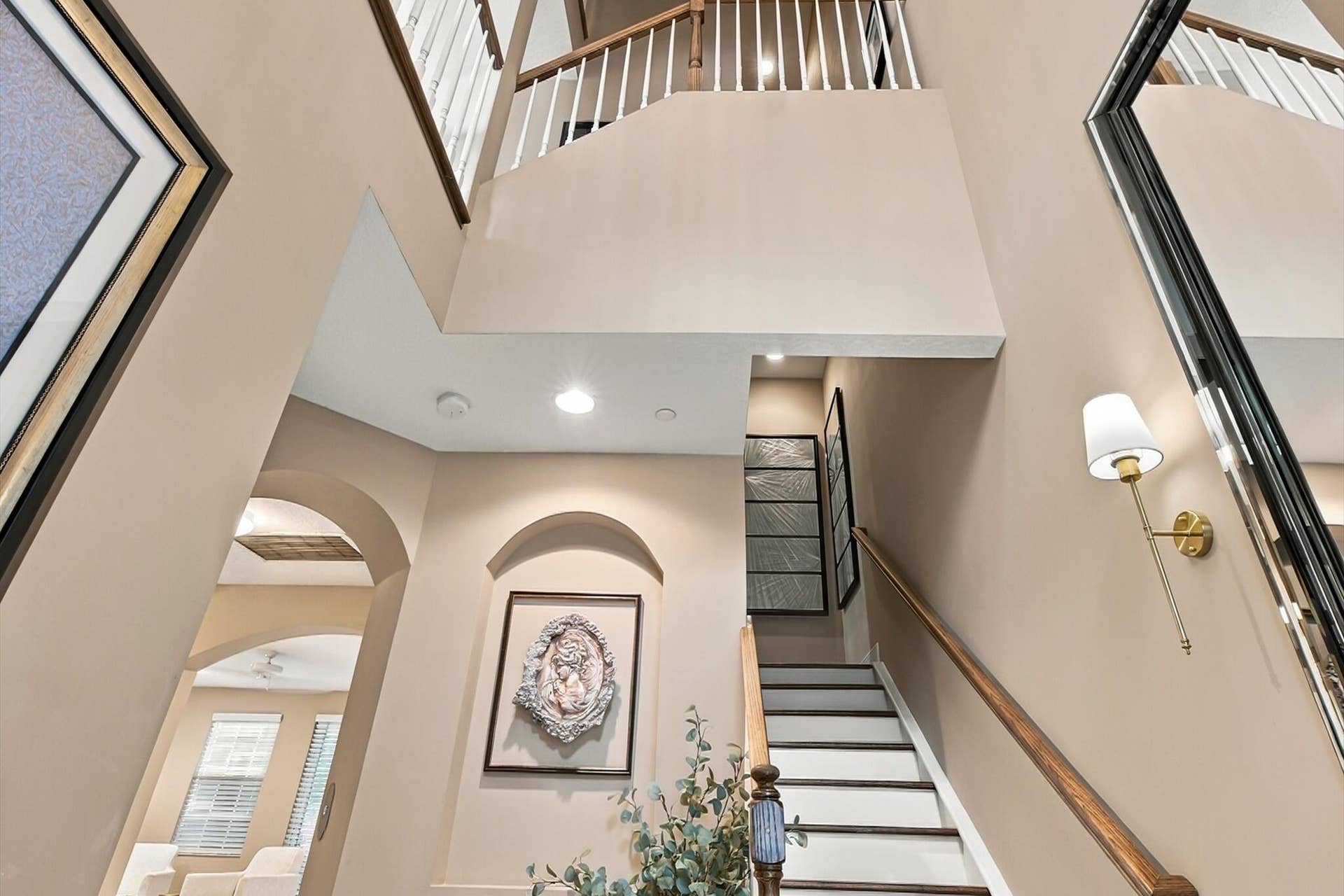 5545 NE Trieste Way, Boca Raton, FL 33487 Double-height entry featuring an arched recessed wall niche, staircase with a wood handrail and white balusters, and wall-mounted brass lighting