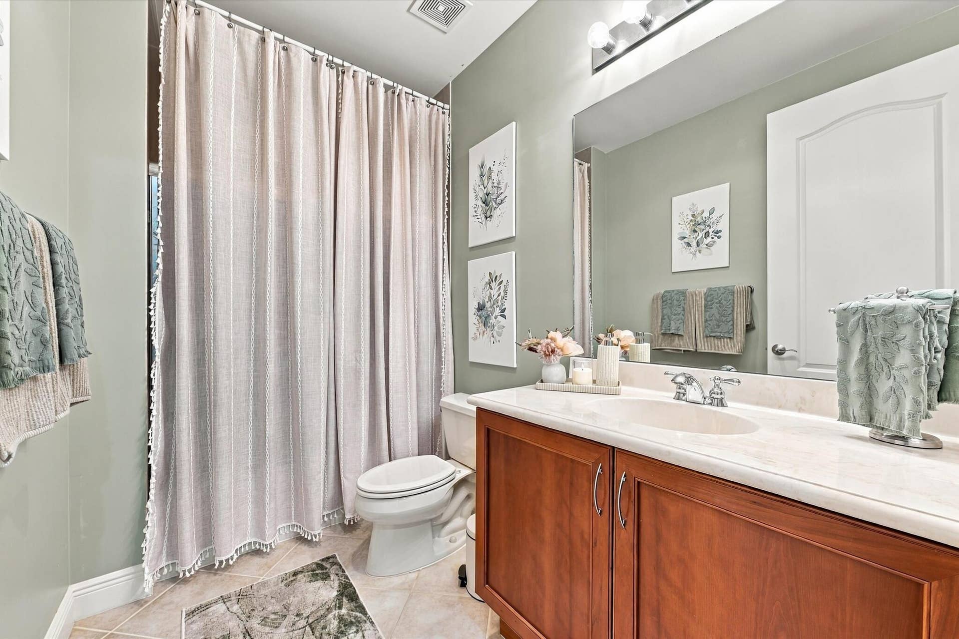 5545 NE Trieste Way, Boca Raton, FL 33487 Full bathroom featuring a wood-finish vanity with a light-toned solid surface countertop, an integrated oval basin, a large wall-mounted mirror, and tile flooring