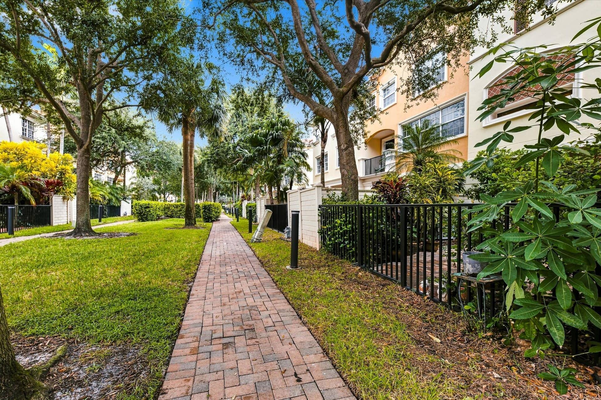 5545 NE Trieste Way, Boca Raton, FL 33487 Brick paver walkway lined with mature trees, established landscaping, and black metal fencing
