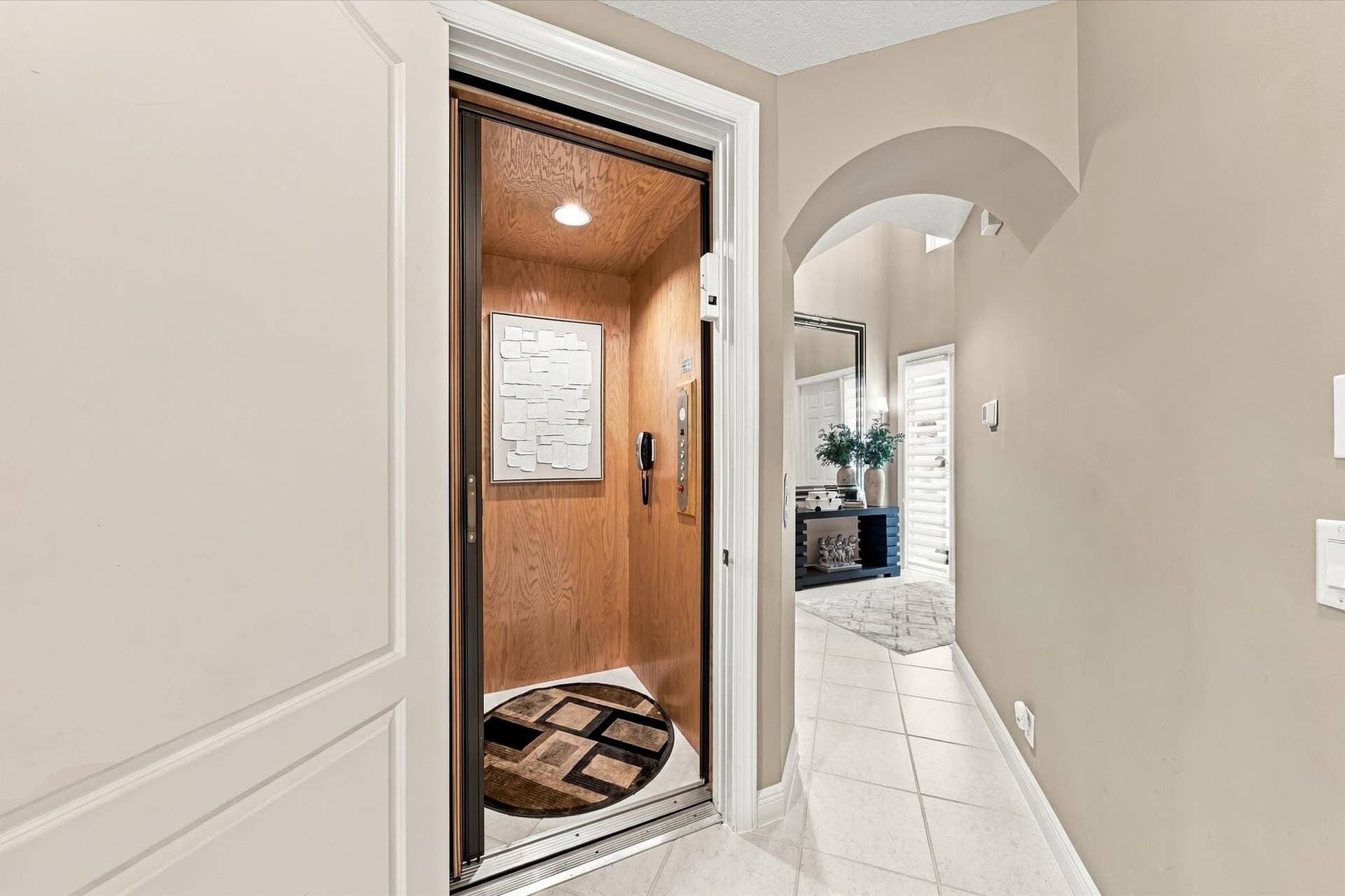 5545 NE Trieste Way, Boca Raton, FL 33487 In-home elevator with wood-paneled interior and recessed lighting, featuring an arched entryway and light-toned tile flooring