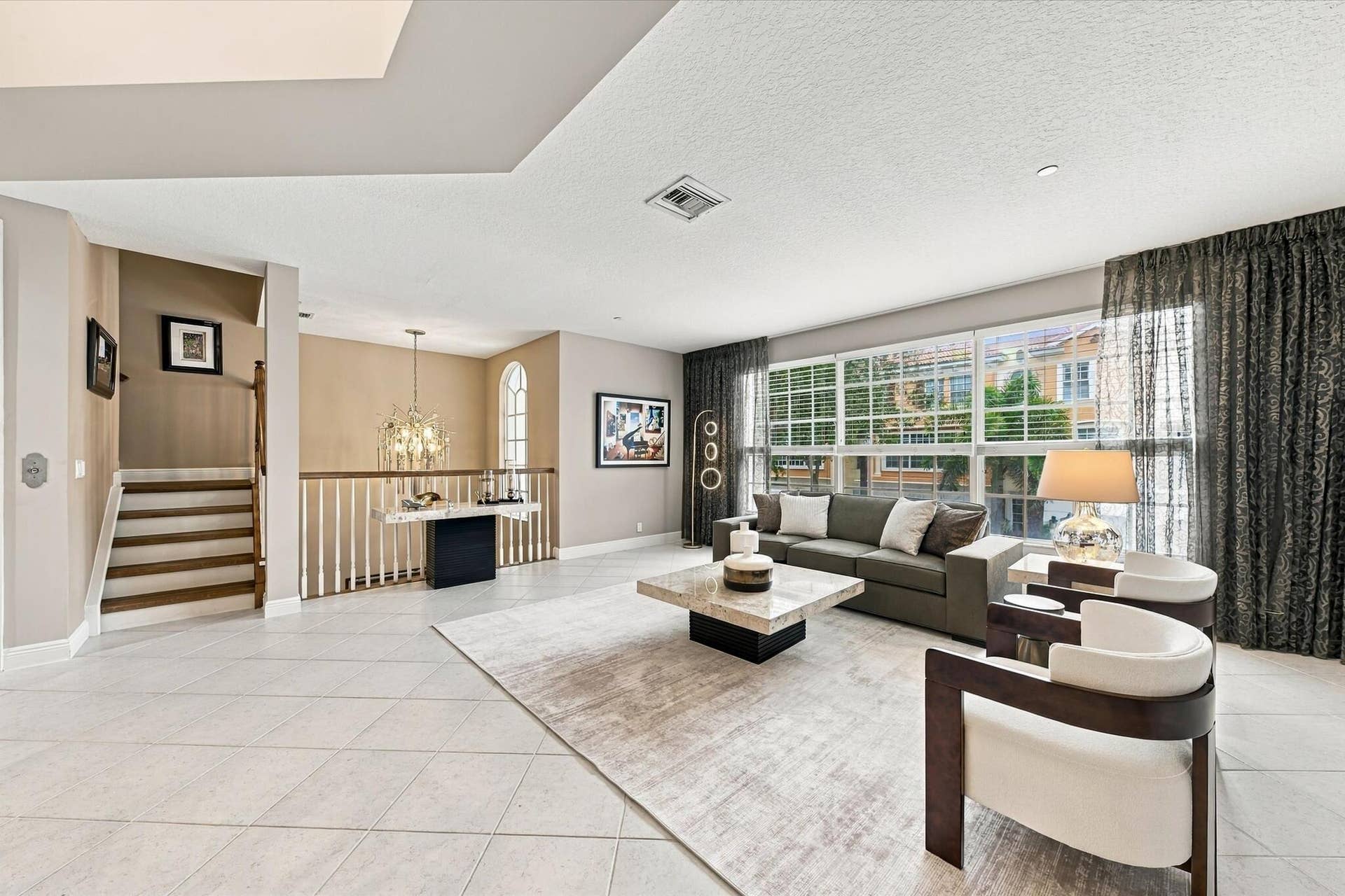 5545 NE Trieste Way, Boca Raton, FL 33487 Open-concept interior featuring large-format tile flooring, multi-pane windows, arched window detail, and a staircase with wood treads and a baluster railing