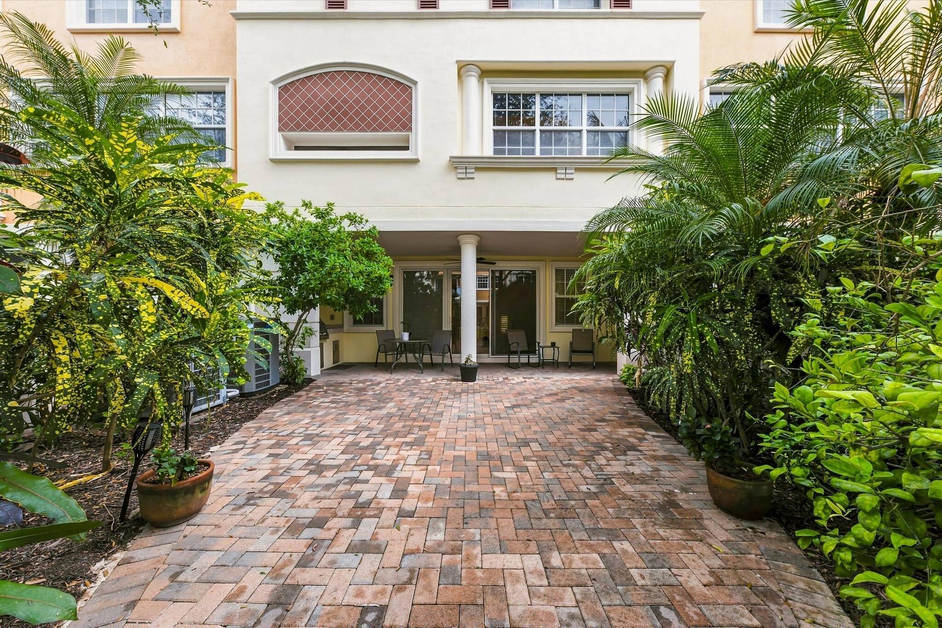 5545 NE Trieste Way, Boca Raton, FL 33487 Brick-paved patio featuring a covered loggia, classical columns, and multi-story stucco facade with decorative stonework detailing