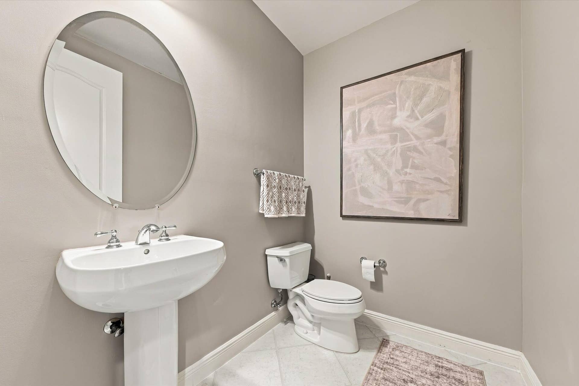 5545 NE Trieste Way, Boca Raton, FL 33487 Oval mirror with a metallic frame, white porcelain pedestal sink, polished chrome widespread faucet, and ceramic tile flooring