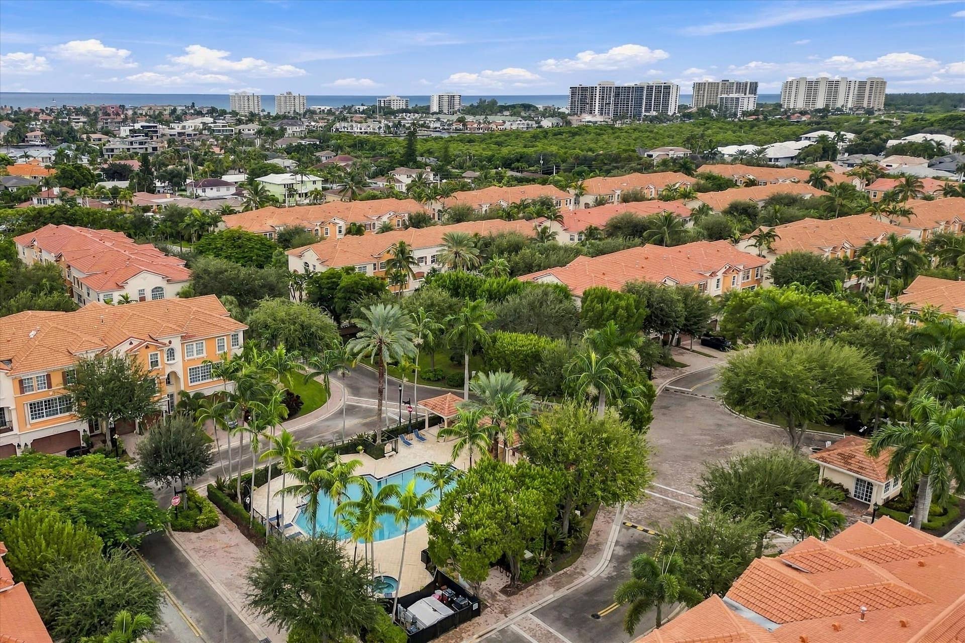 5545 NE Trieste Way, Boca Raton, FL 33487 Aerial perspective featuring tile-roofed architecture, palm-lined landscaping, a communal swimming pool, and a coastal horizon
