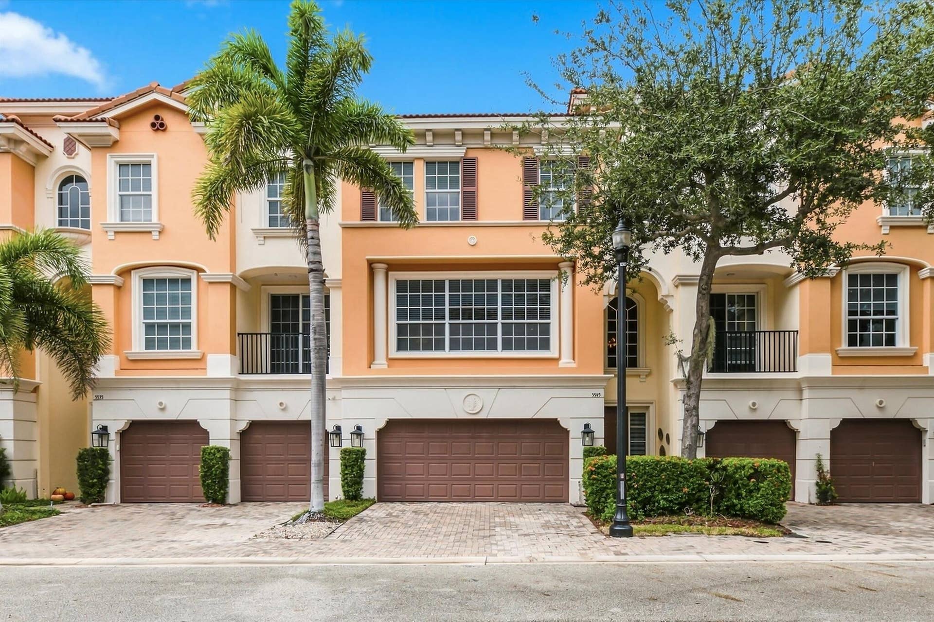 5545 NE Trieste Way, Boca Raton, FL 33487 Mediterranean-style exterior featuring a multi-level facade, arched window detailing, wrought iron balcony railings, paved driveway, and attached multi-car garage