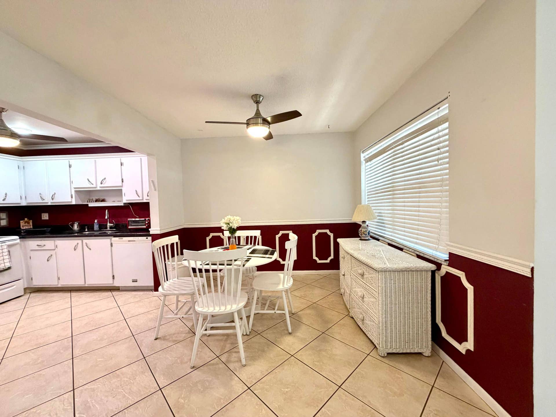 Dining area featuring diamond-pattern tile flooring, dual-tone wall paint with applied wainscoting, and a central ceiling fan with integrated lighting