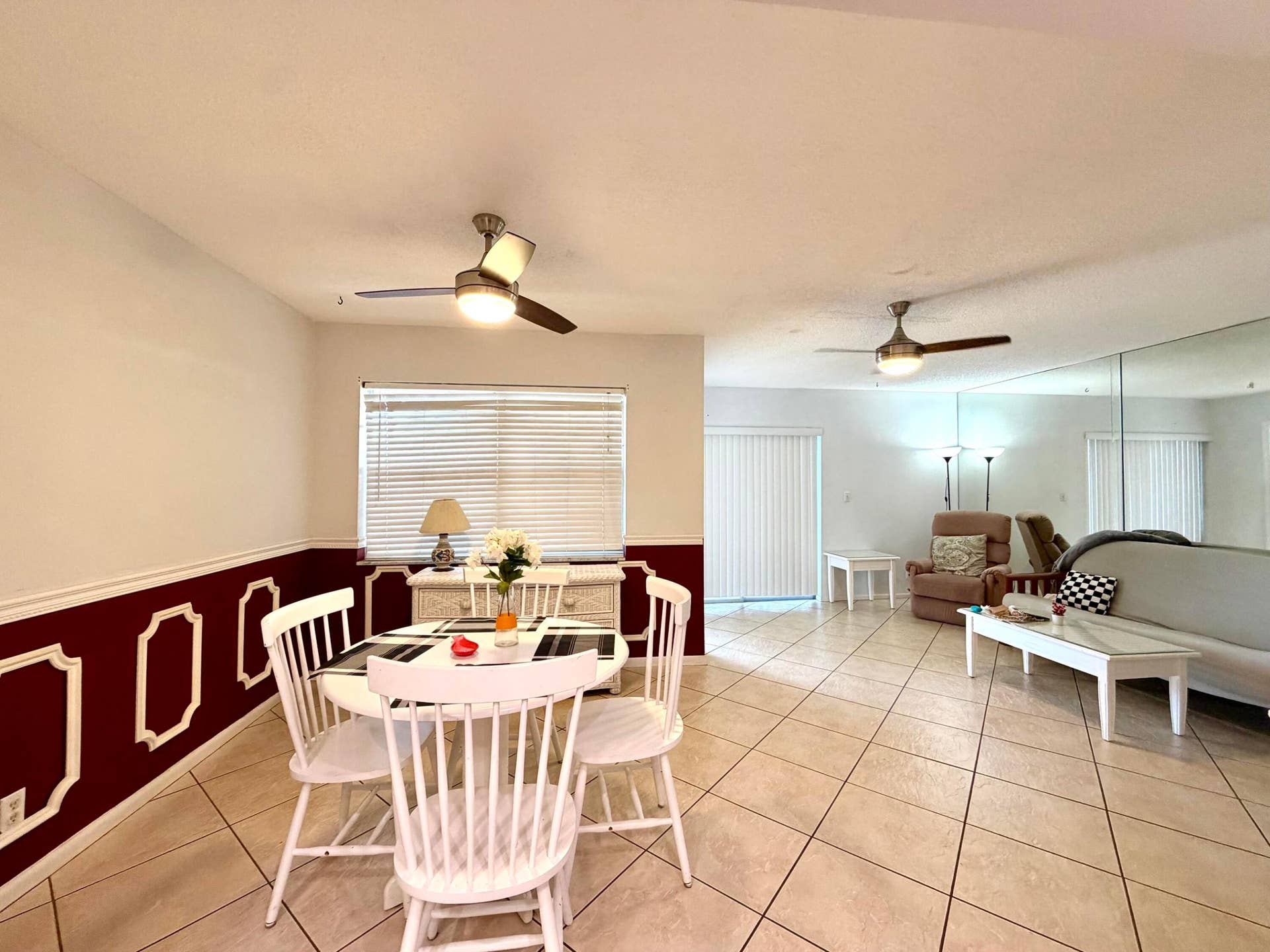 Ceramic tile flooring, two ceiling-mounted light fixtures with integrated fans, wainscoting with decorative millwork, mirrored wall paneling, and sliding glass door