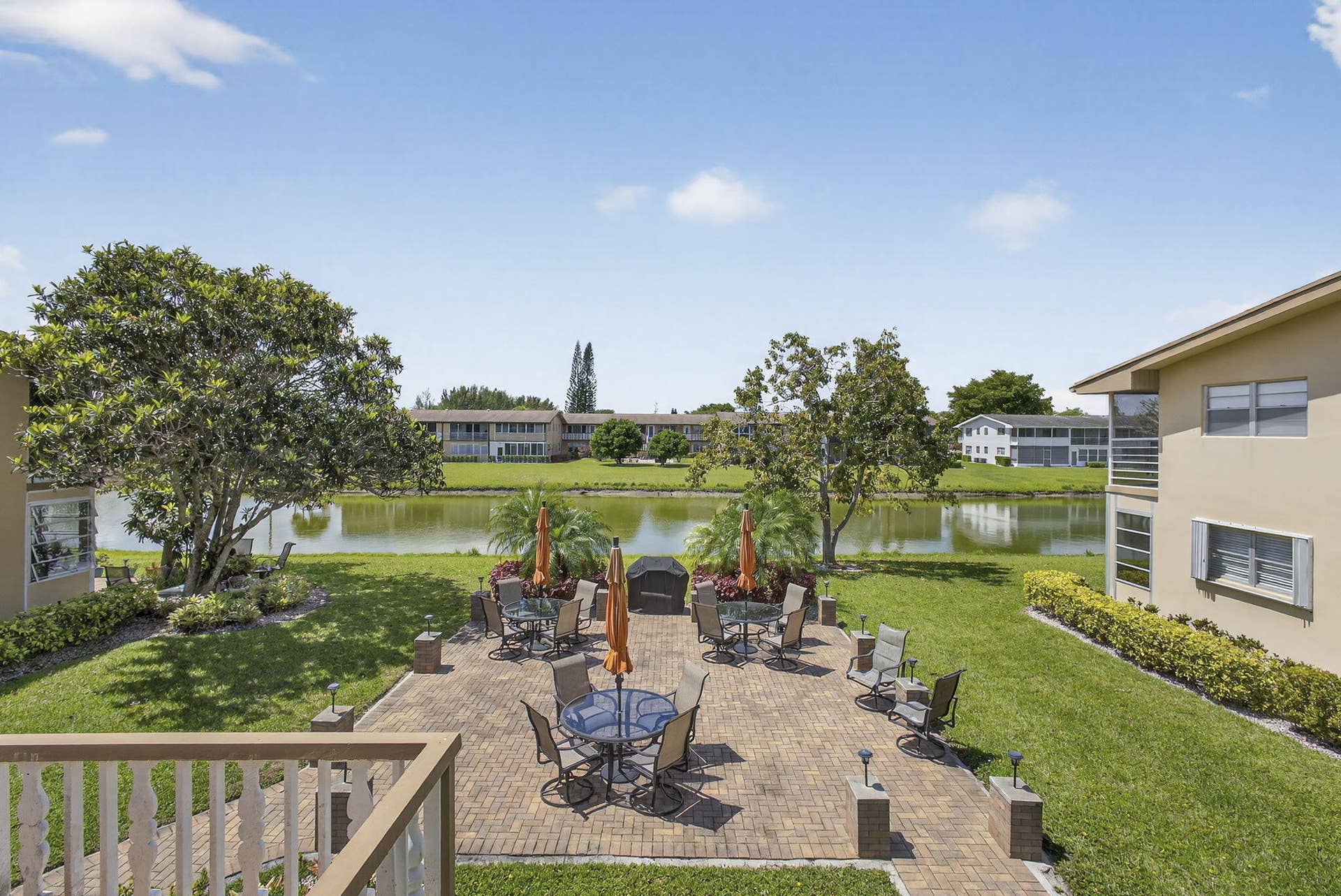 Waterfront brick paver patio featuring low-voltage landscape lighting, manicured lawn, and mature trees