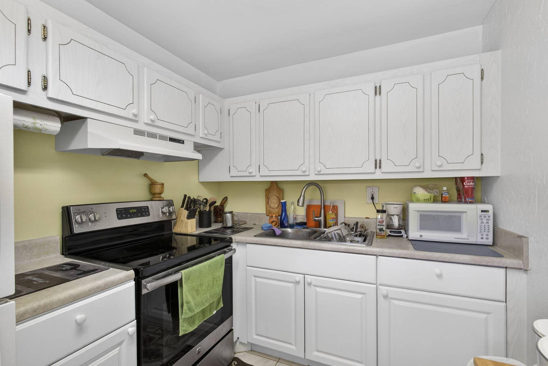 White cabinetry with recessed detailing, stainless steel range, undermount kitchen sink, neutral-toned countertops, and range hood