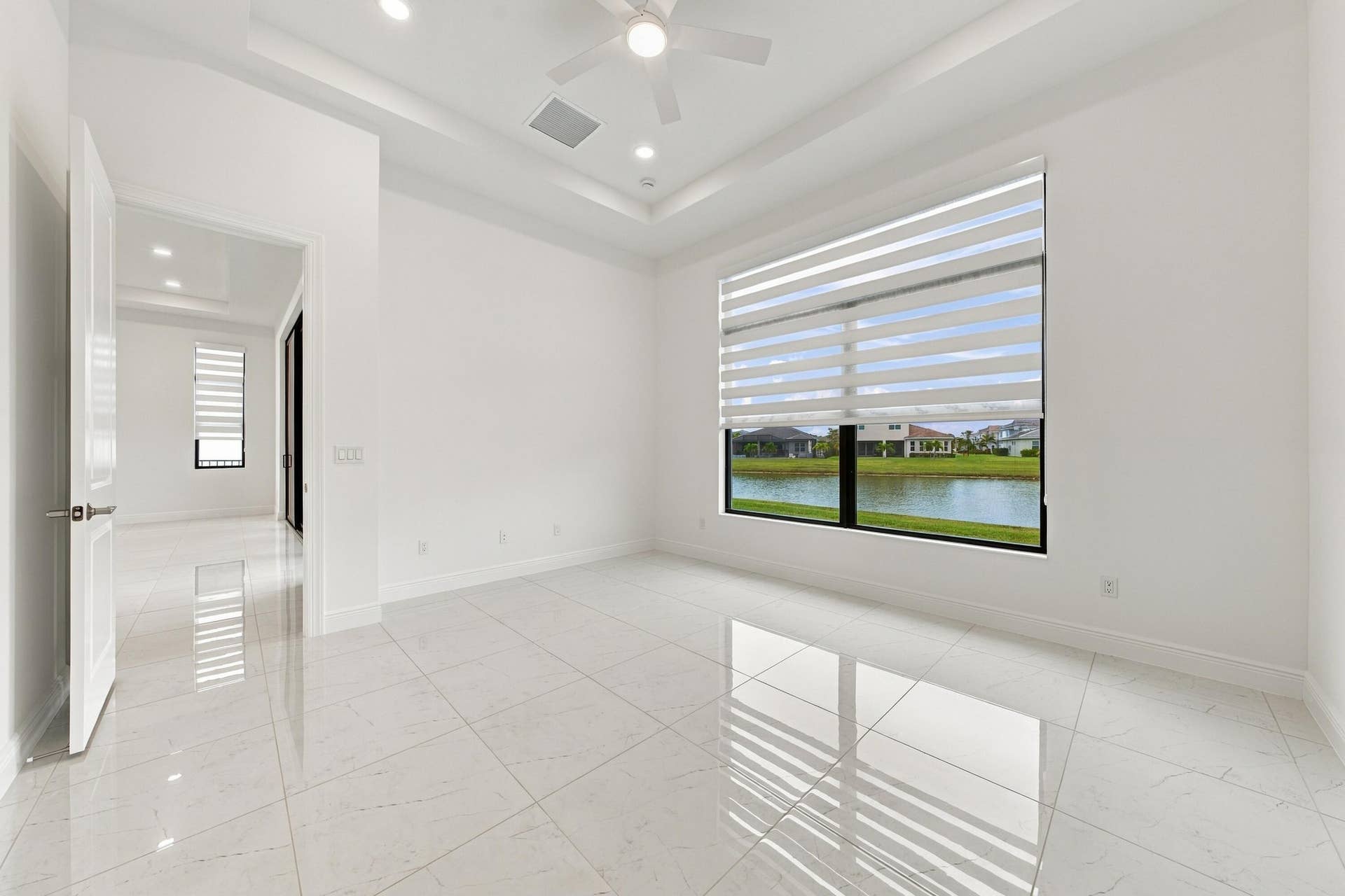 4931 Rivo Alto Circle, Westlake, FL 33470 Primary suite with tray ceiling, ceiling fan and zebra blinds with lakefront views