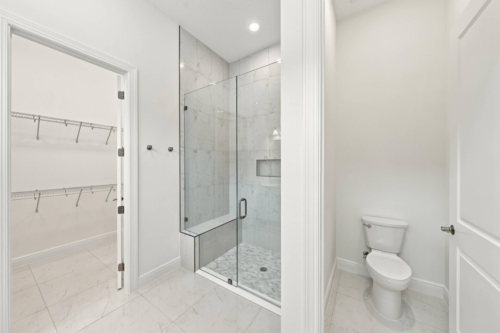 4931 Rivo Alto Circle, Westlake, FL 33470 Primary bathroom frameless 96 inch glass shower with bench and upgraded tile to the ceiling with soft pebble shower floor, walk-in closet