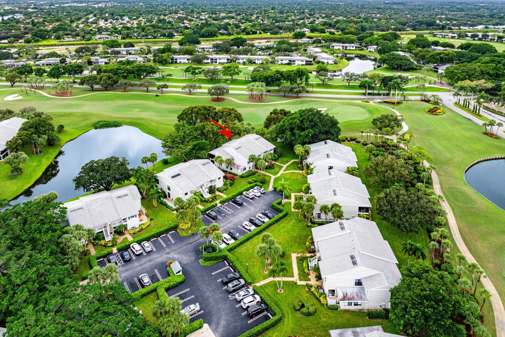53 EASTGATE Drive, #B, Boynton Beach, FL 33436 Aerial perspective of a multi-unit residential complex featuring light-toned exteriors, pitched roofs, paved surface parking, and manicured grounds integrated with water features and golf course fairways