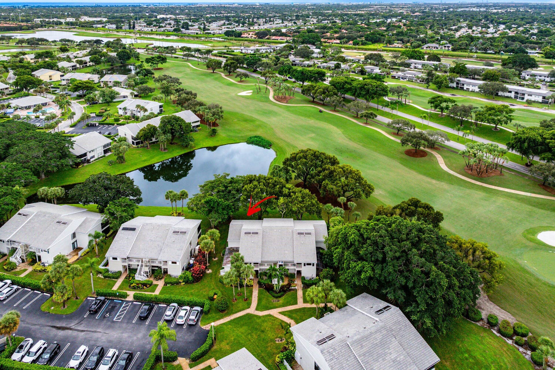 53 EASTGATE Drive, #B, Boynton Beach, FL 33436 Aerial perspective featuring multi-story residential buildings with light-toned shingle roofing, positioned along a water feature and bordering an expansive manicured green space